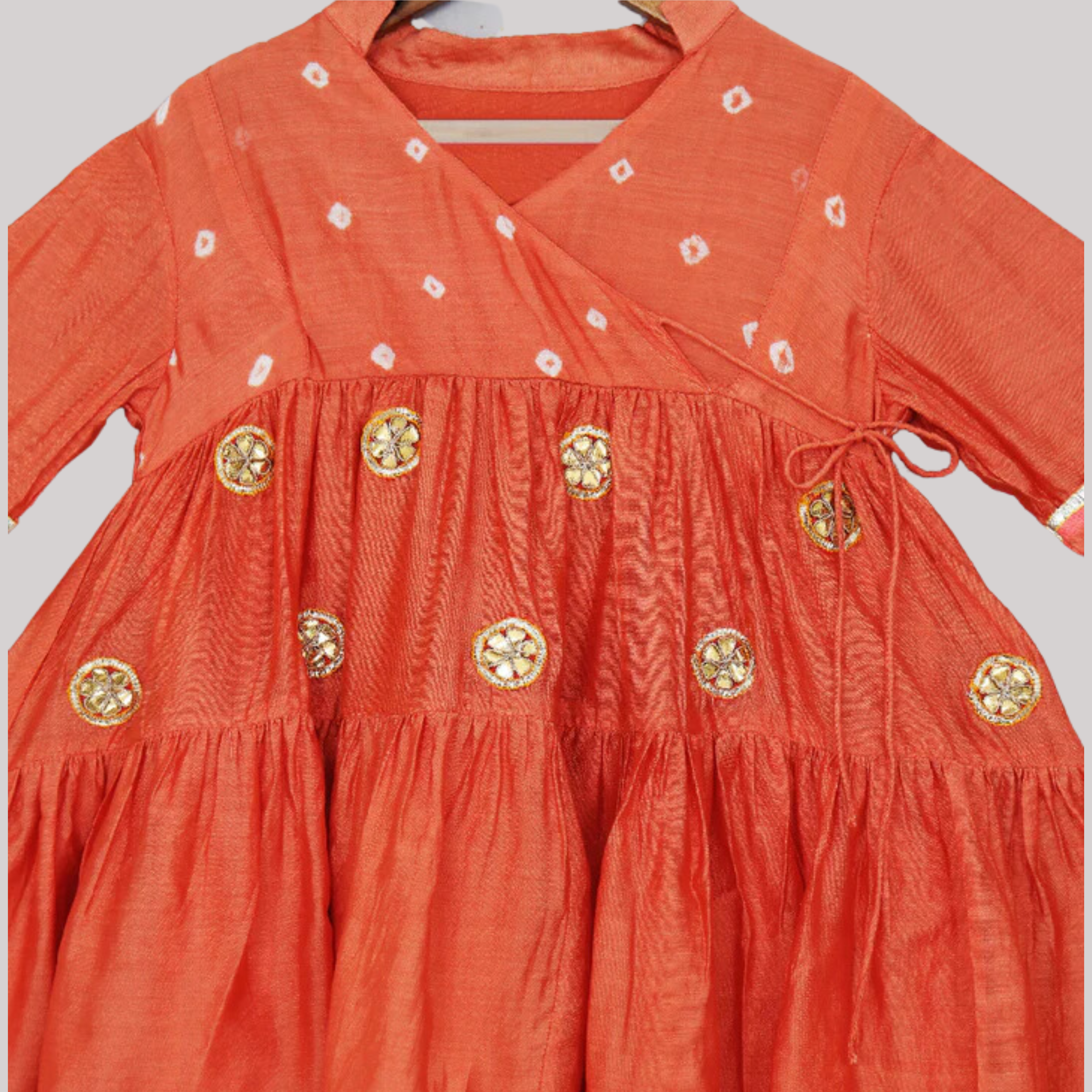 Little girl in a vibrant orange ethnic dress adorned with laces and gota flowers.